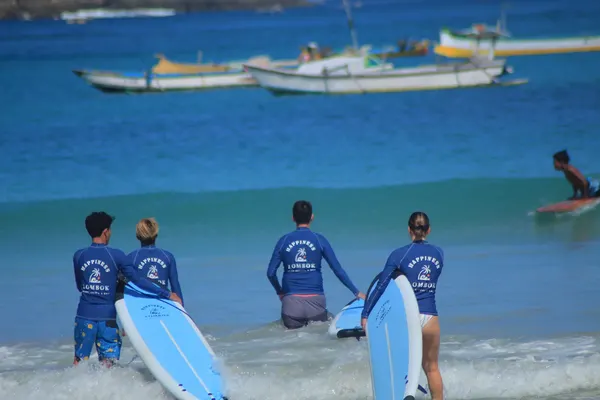 Surf school students in Happiness Lombok rashguards entering the ocean with surfboards at Kuta Lombok